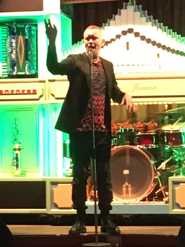Pieter zingt op het podium voor een orkestpodium met drumstel